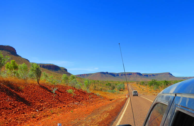 Een auto rijd door de Australische outback, je ziet de weg tussen de bergen en bomen