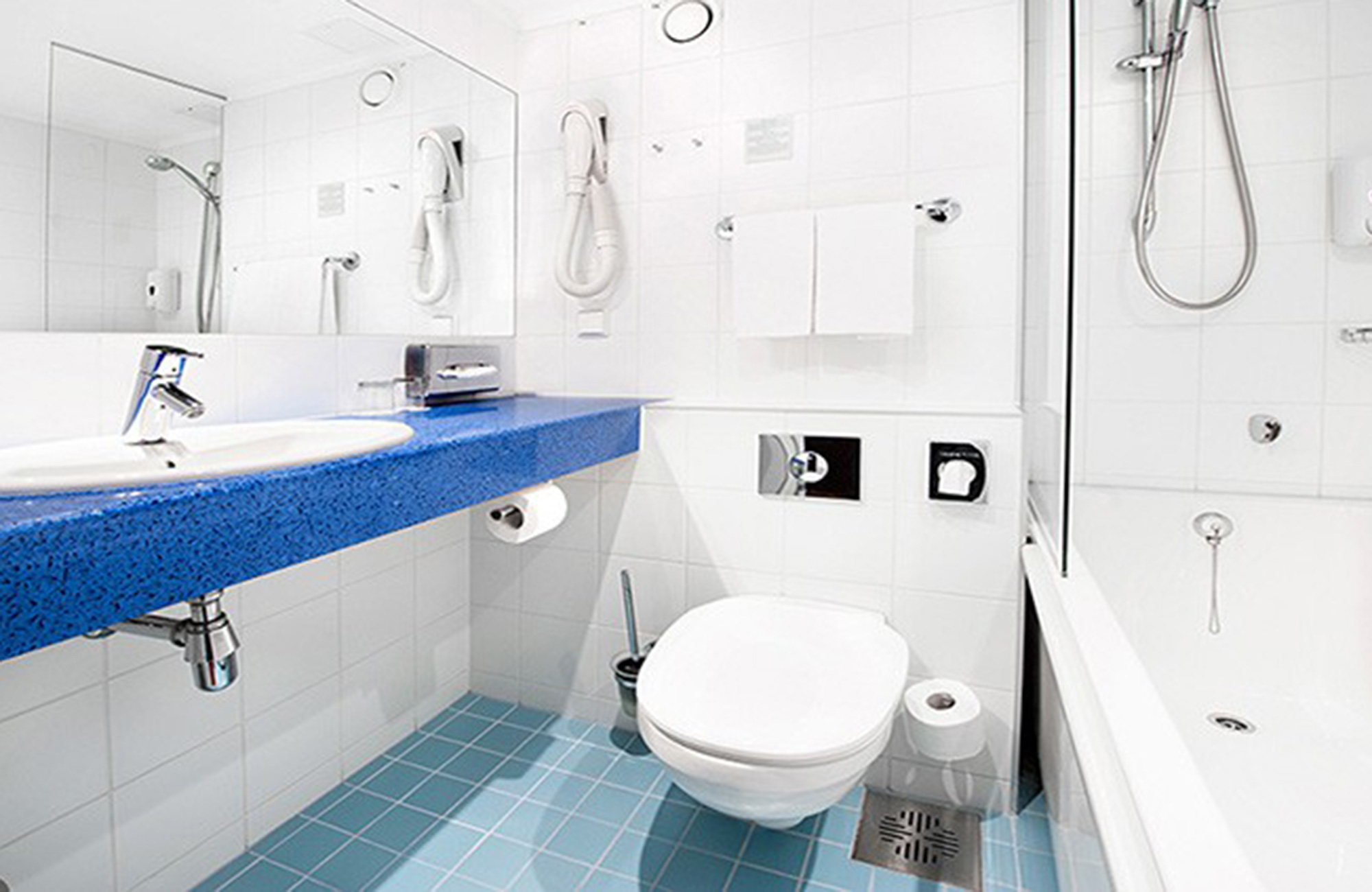Moderne badkamer in Hotel l'Ermitage Tallinn met blauwe wastafel, toilet en een wit betegeld bad met douche.