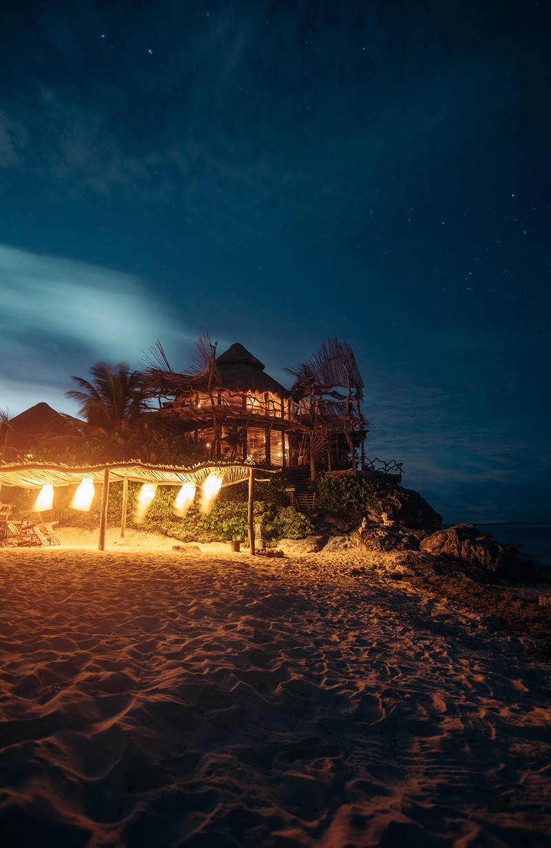 Sfeervol verlichte strandhut in Mexico die op een rotsachtige verhoging ligt en omgeven is door zand en warm gele lampem