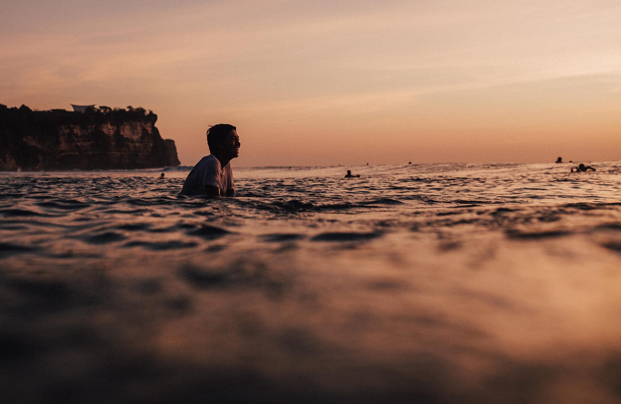 Surfer in het water in Uluwatu, Bali tijdens zonsondergang