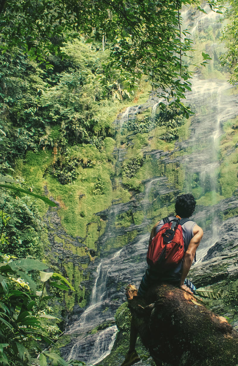 Backpacker sitting on a tree log in front of a waterfall in Costa Rica