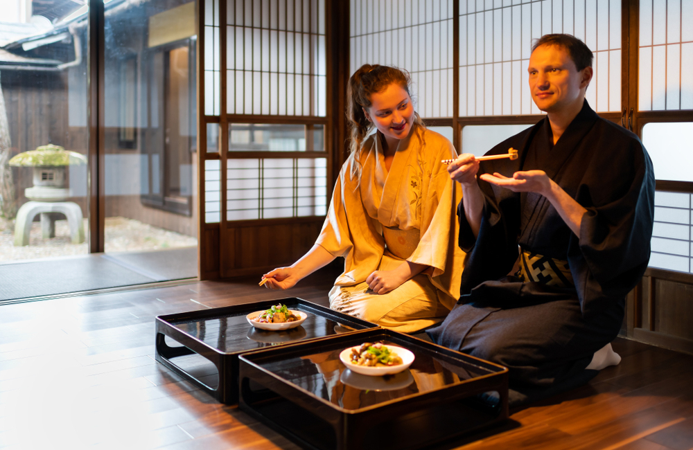 Een koppel in traditionele Japanse kleding (yukata) geniet van een authentiek diner in een klassieke Japanse ryokan, met shoji-schermen en zicht op een binnentuin. - KILROY