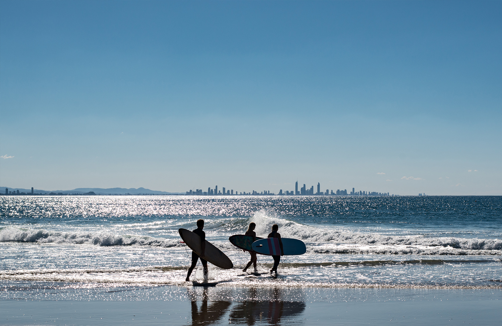 Drie surfers wandelen met hun surfboard langs een Australisch strand
