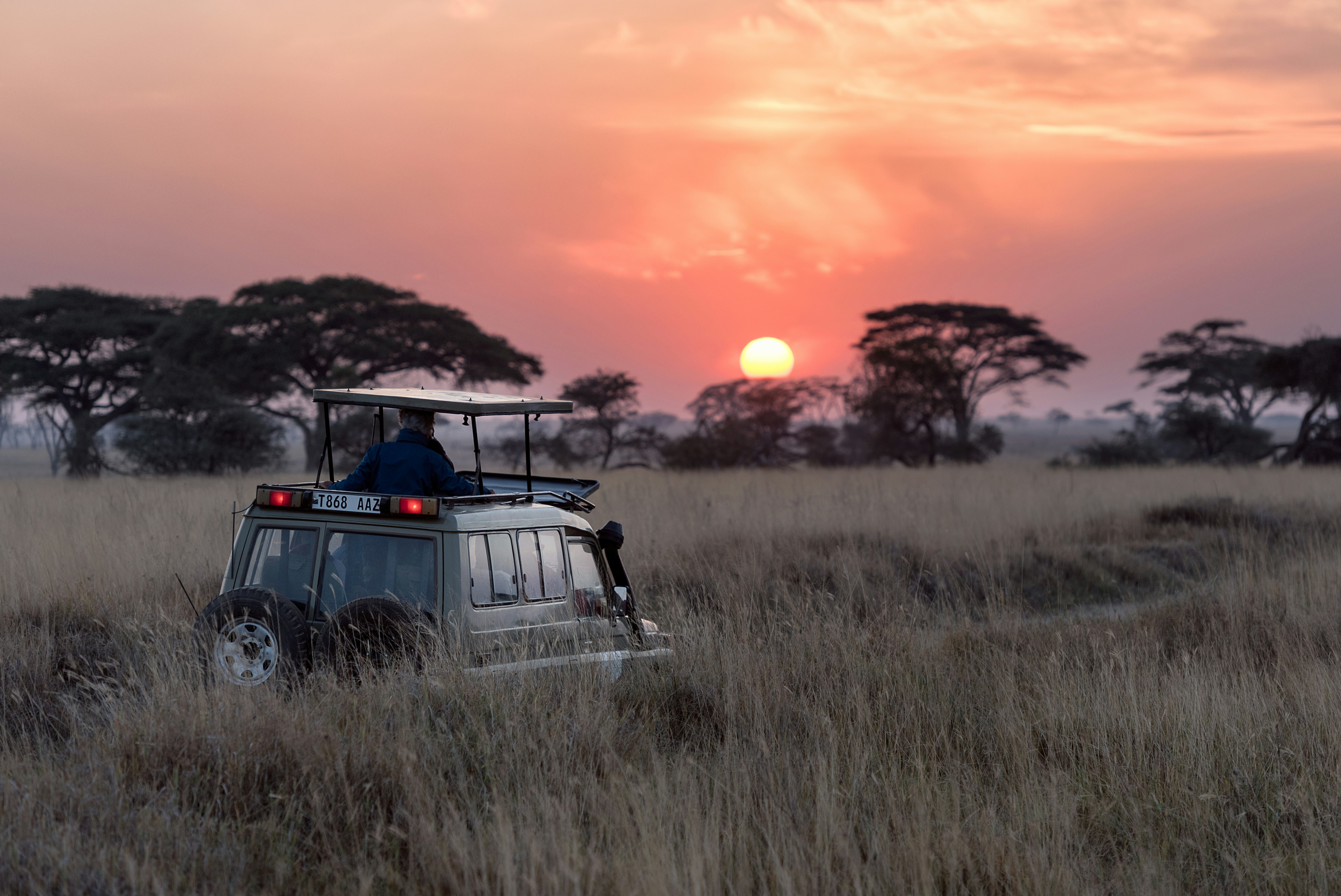 Een safari-jeep op de uitgestrekte savanne van de Serengeti in Tanzania, uitkijkend over een indrukwekkende roze zonsondergang.