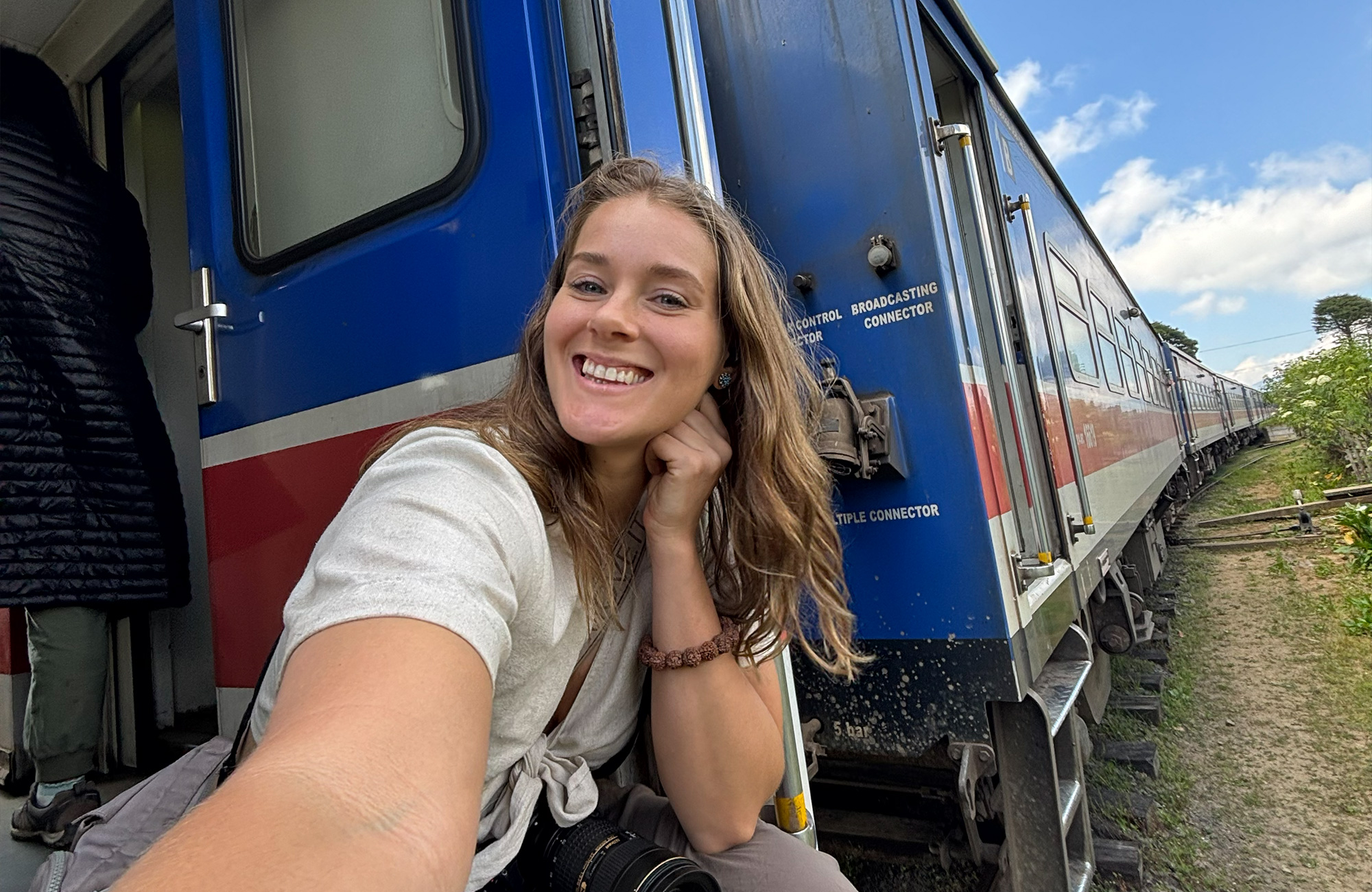 Een lachend meisje neemt een selfie terwijl ze uit de iconische blauwe trein in Ella, Sri Lanka leunt tijdens een zonnige reis.