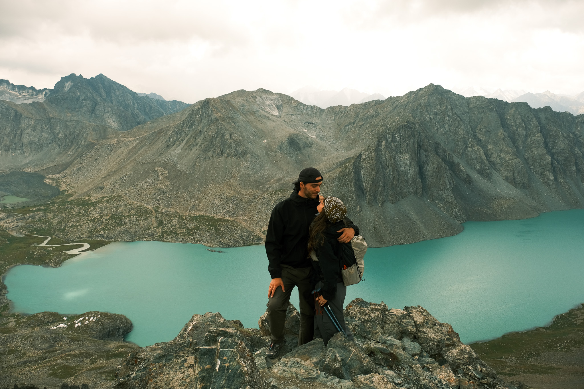 Een koppel omarmt elkaar op een bergtop met uitzicht op het turquoise Ala-Kul meer in Kirgizië.