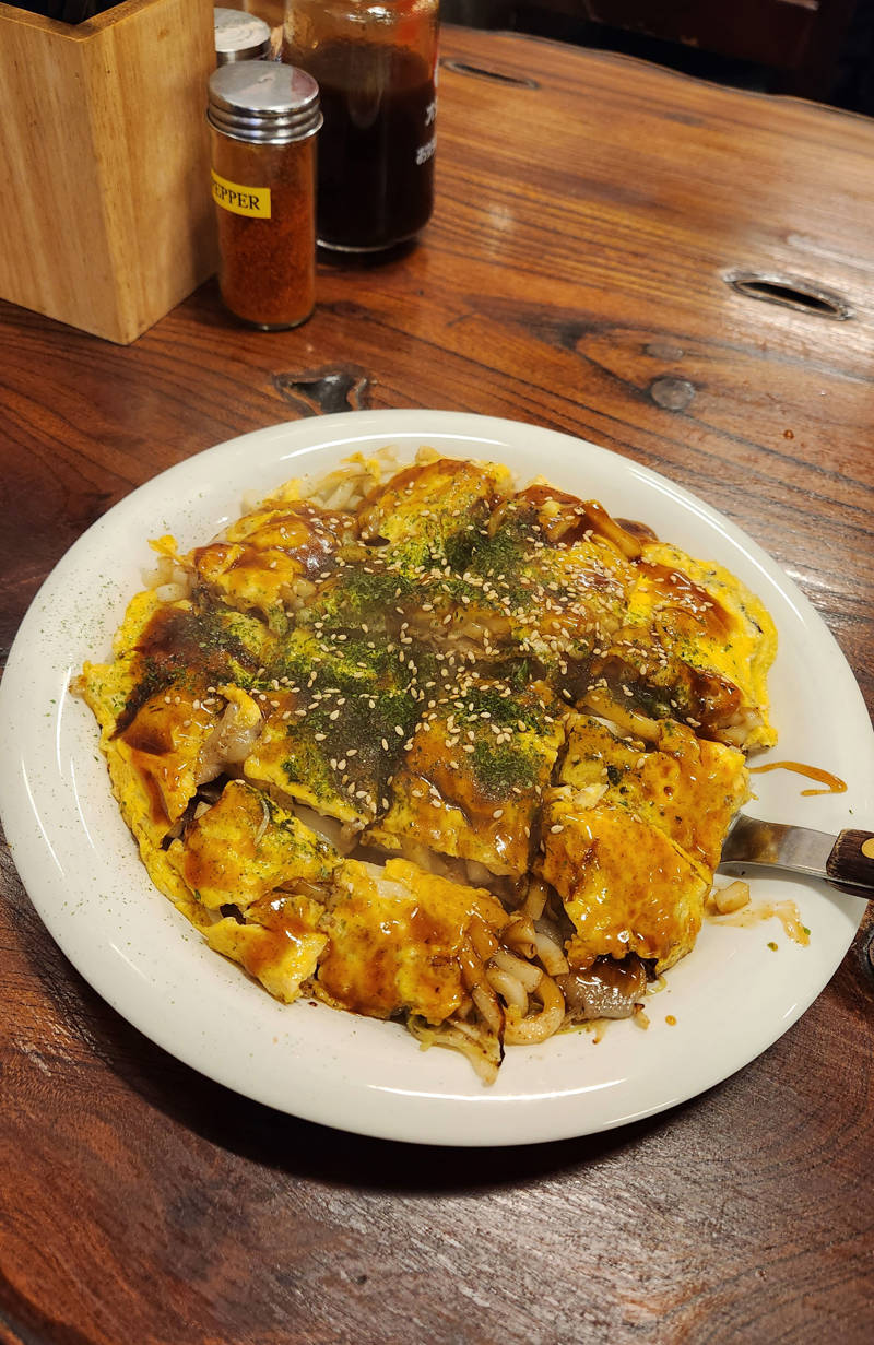 Gerecht okonomiyaki, een zoete pannekoek/omelet met noedels, groenten en saus.