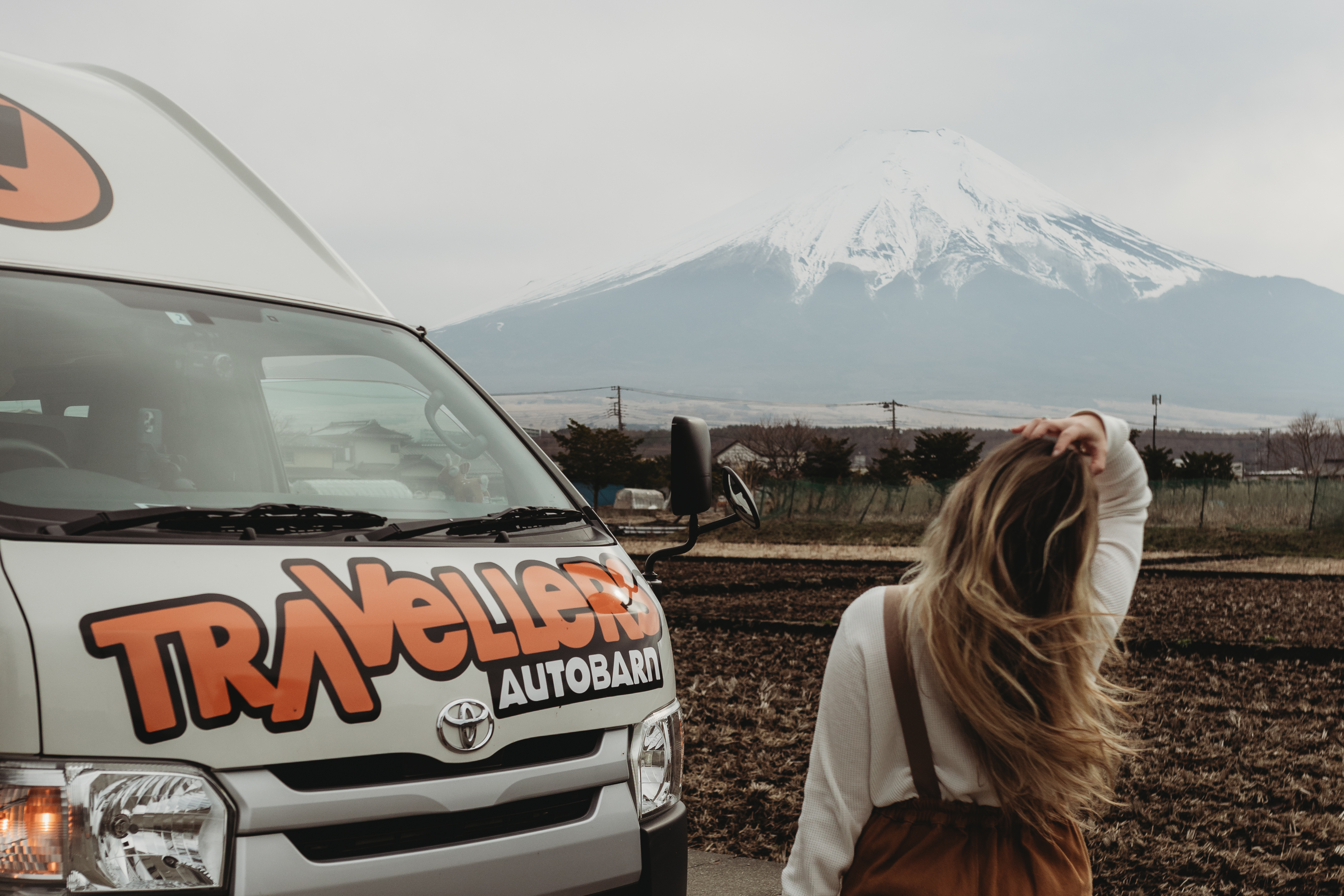 Campervan van Travellers Autobarn met een vrouw die uitkijkt op een berg met besneeuwde top