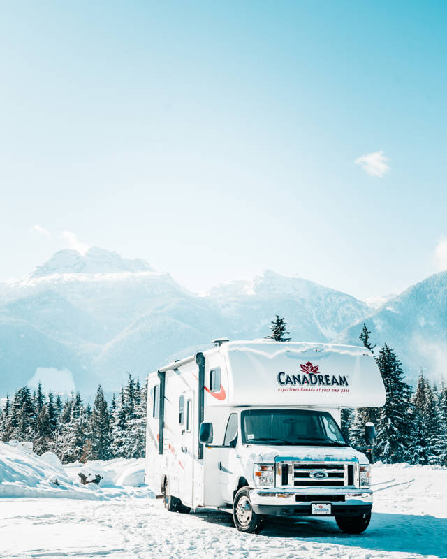 Maxi Motorhome van Canadream rijdt op een besneeuwde weg in Canada tussen de bergen en bomen