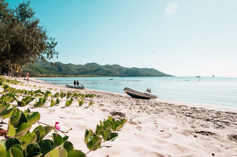 Een zandstrand met twee rubberboten, groene heuvels en een blauwe oceaan op Magnetic Island
