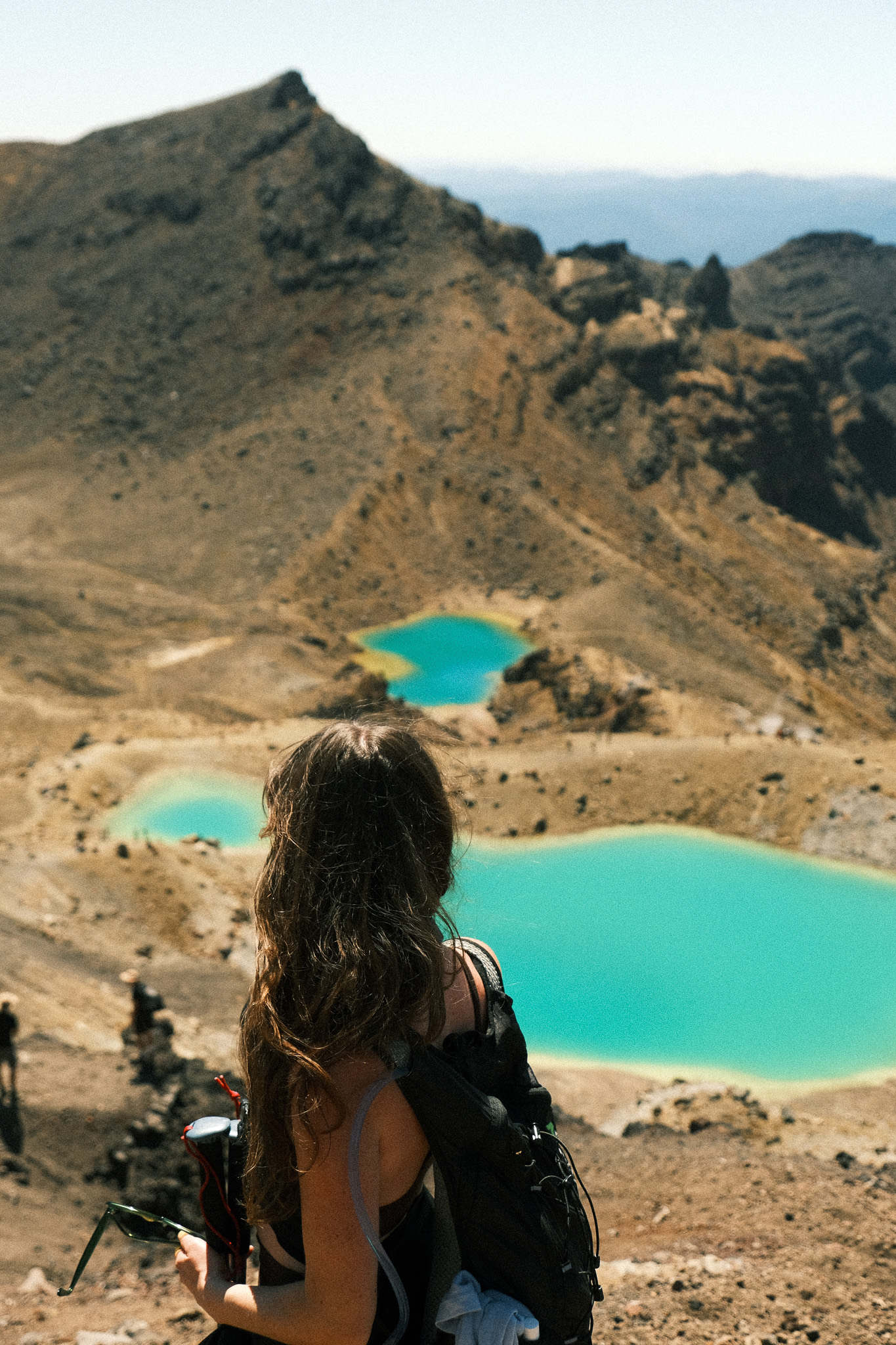 Persoon kijkt uit over felblauwe vulkanische meren in een bergachtig landschap van Tongariro National Park in Nieuw-Zeeland.